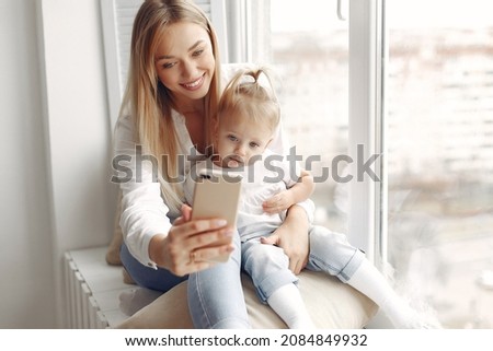 Mother and little daughter spend time together sitting on the windowsill.