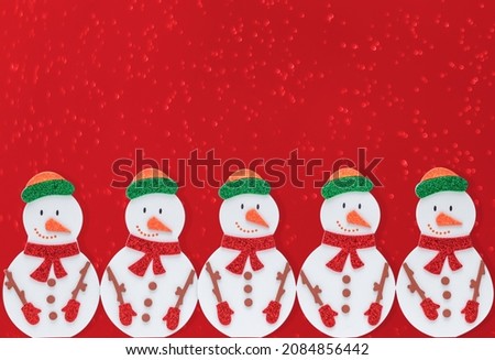 New Year's decor snowmen made of paper stand in a row on a red heterogeneous background.