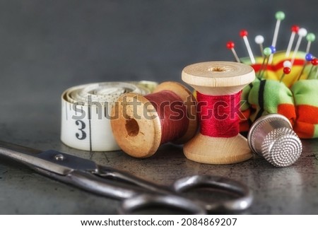 Multicolored threads on a wooden spool, sewing needle with scissors thimble and tailor's tape on an old surface. Sewing thread background. Retro style. selective focus 
