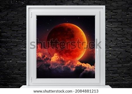 Picture of a white framed window on a black brick wall. In the picture behind the window is a picture of orange moon in the clouds Suitable for use in advertising media .