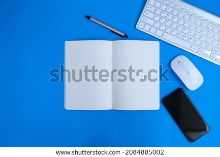 On a blue background, a flat lay top view mockup photo of a working place with a laptop, smartphone, money and notebook is shown. Concept of a working desk with a blue background.