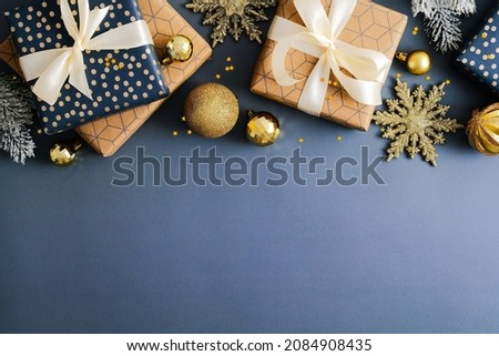 Christmas frame top border made of Xmas gift boxes, gold baubles , snowflakes on dark blue background. Flat lay, top view, copy space. Elegant Christmas card design.