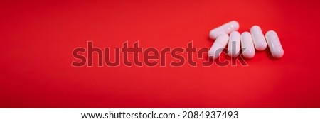 White drug capsules on colored red paper background. Macro close up pill medication. Book cover. Approved medicine drugs use. Pharmacy concept. Copy space. New Year Calendar Mock up design template.