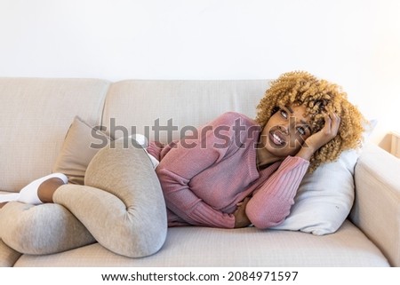 Cropped shot of an attractive young woman lying on her sofa alone and suffering from period cramps at home. Ouch! My tummy! Woman with menstrual pain. Woman with hands on stomach suffering from pain