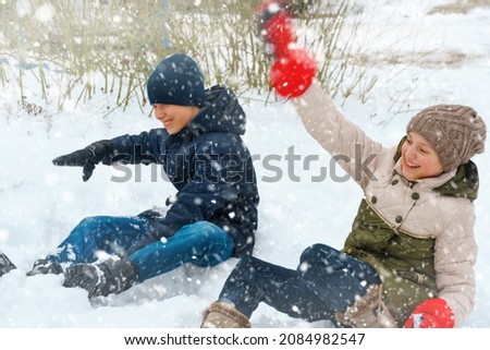 a girl and a boy are playing snowballs outside, beautiful winter weather and white snow around