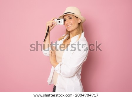 Happy smiling young woman wearing straw hat isolated over pink background with a camera in her hands
