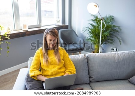 Smiling young woman using laptop, sitting on couch at home, beautiful girl shopping or chatting online in social network, having fun, watching movie, freelancer working on computer project