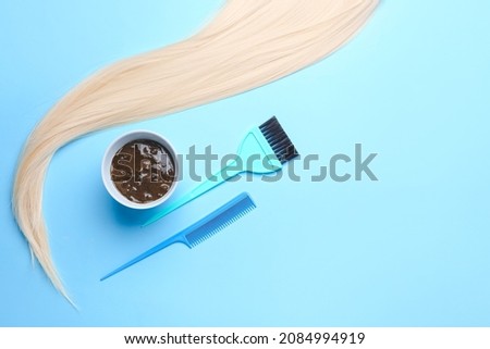 Bowl with henna, hair and hairdresser's supplies on color background