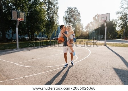 summer holidays, love and people concept - happy young couple with ball kissing on basketball playground