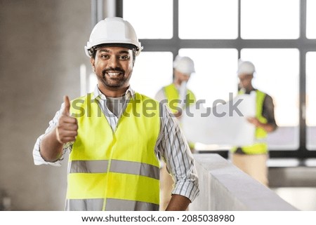 architecture, construction business and building concept - happy smiling male architect in helmet and safety west at office showing thumbs up