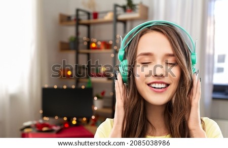 music, christmas and people concept - happy young woman or teenage girl with headphones at home over decorated living room background