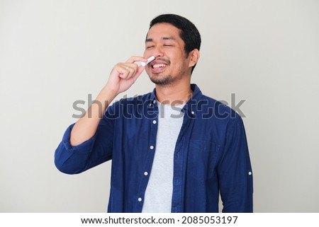 Adult Asian man showing relieved expression when using nasal stick inhaler Royalty-Free Stock Photo #2085053197