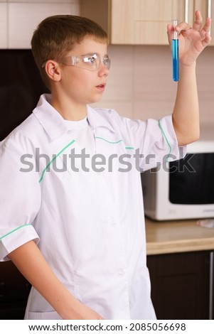 a white boy in a white coat looks at a test tube with a blue solution. Home laboratory. Teaching chemistry at home.