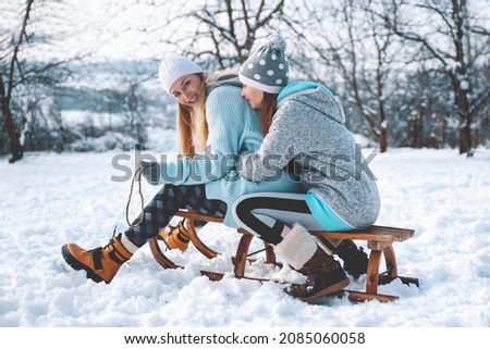 Woman Sledding with her Daughter in snowy day Outdoors. Mother and teenage Girl having fun in Winter Park In Mountain
