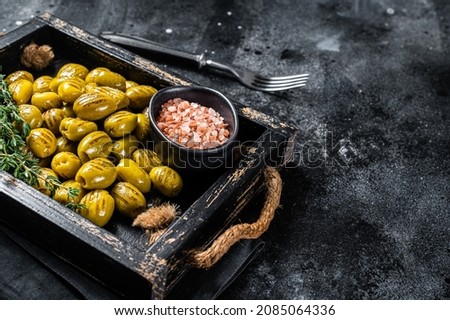 Greek Grilled olives with garlic, olive oil and spices in wooden tray. Black background. Top view. Copy space