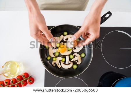 Cropped photo cooking man adding sliced vegetables mushrooms on frying pan making omelette