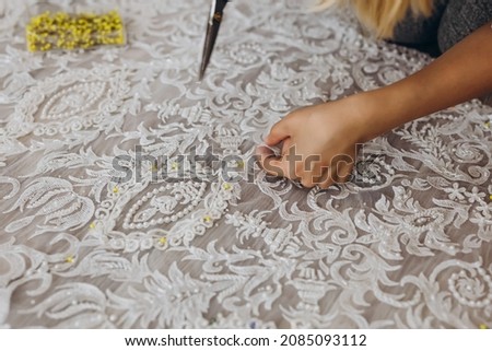 A professional dressmaker is correcting a ornament with scissors. She has scissors in her right hand. There are a lot of yellow needles near her.