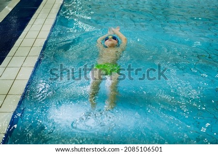 little caucasian boy wearing goggles swimming the backstroke in a pool. High quality photo