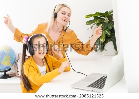 Mother and her girl listening to music on laptop. They sitting in living room. Natural light ambient.