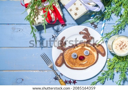Christmas New Year morning breakfast, kids festive brunch snack. Funny reindeer pancakes made with with berries, chocolate and vanilla dough