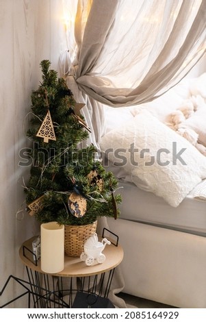 The bedroom decorated by Christmas. Cozy light interior: plaid, wooden bed and chair. In the room there is a New Year's fir-tree decorated with toys and garlands