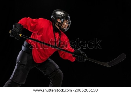 Motivated sportsman. Professional female hockey player training in special uniform with helmet isolated on black background. Winning game. Concept of sport, action, movement, health. Copy space for ad