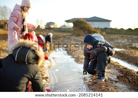 Group of children playing with thin ice puddles formed on the frozen soil in winter. Kids having fun in winter. Winter activities for kids.