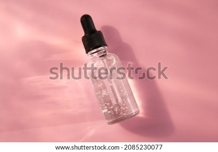Transparent glass dropper bottle with air bubbles on pink background in sunlight. Pipette with fluid hyaluronic acid, serum, retinol. Cosmetics and healthcare concept Flat lay. Luxury beauty product