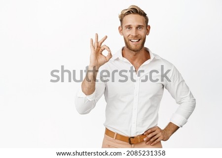 Image of handsome adult man in stylish clothes say okay, give permission, make OK gesture and smiling pleased, standing over white background