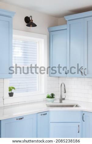 Detail of a kitchen with light blue cabinets, white granite countertop, subway tile backsplash, and a light hanging above a window. Royalty-Free Stock Photo #2085238186
