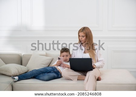 Mom watches her son read a book over the phone. Mom and son spend time at home.