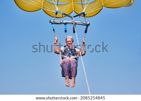 Senior white woman with gray hair is fearless and fun parasailing. Extreme sports concept. Close up Royalty-Free Stock Photo #2085254845