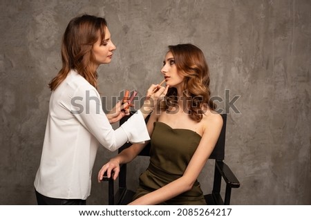a professional makeup artist in a white blouse does makeup for a model's girlfriend on a gray background with a place for text