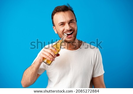 Cheerful young man in t-shirt holding beer bottle against blue background