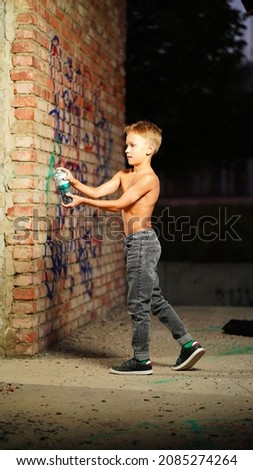 the boy paints with spray paint in the city in the evening