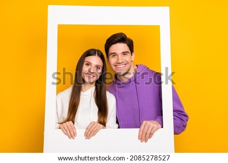Photo of attractive lady handsome guy hold picture frame beaming toothy smile isolated on yellow color background