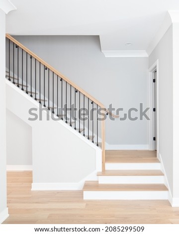 A staircase going up with natural wood steps and handrails, white risers, and wrought iron spindles. Royalty-Free Stock Photo #2085299509