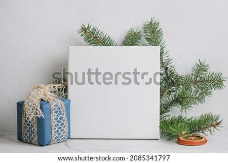 Blank wrapped canvas and Christmas gift box on table. Copy space for message or photo. Mockup poster in white interior, Christmas concept. 
