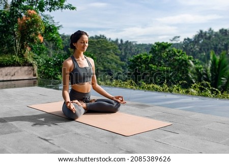 
A beautiful girl practices yoga by the pool in the morning in Bali, Indonesia. Young woman in sportswear near the infinity pool against the backdrop of a tropical landscape. Royalty-Free Stock Photo #2085389626