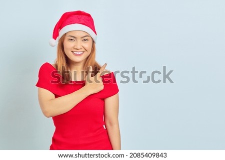 Portrait of smiling young Asian woman pointing to copy space with finger on white background