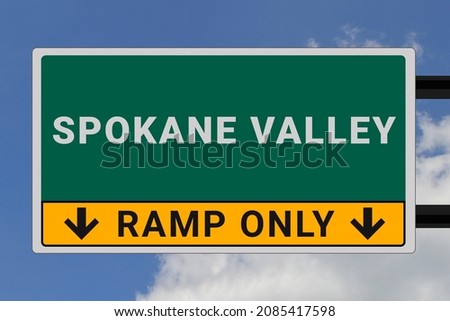 Spokane Valley logo. Spokane Valley lettering on a road sign. Signpost at entrance to Spokane Valley, USA. Green pointer in American style. Road sign in the United States of America. Sky in background