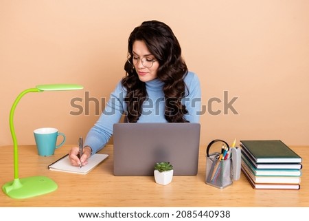 Photo of intelligent cute lady dressed blue pullover glasses writing book working gadget isolated beige color background