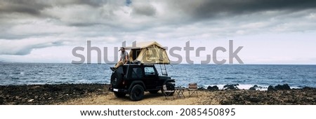 Banner travel header with man sitting on the roof of the car with camping tent having relax time and enjoying adventure travel lifestyle or alternative free vacation Royalty-Free Stock Photo #2085450895