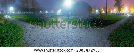 The path diverges into three different directions in the foggy twilight and the light of night lanterns with different color temperatures