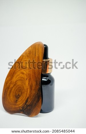 a bottle with a cosmetic product made of dark glass and a wooden gouache scraper on a white background. natural cosmetic. eco-friendly personal care