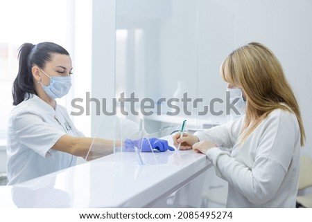 A receptionist in a modern hospital helps a young female patient fill out documents. Consent to the processing of personal data Royalty-Free Stock Photo #2085495274