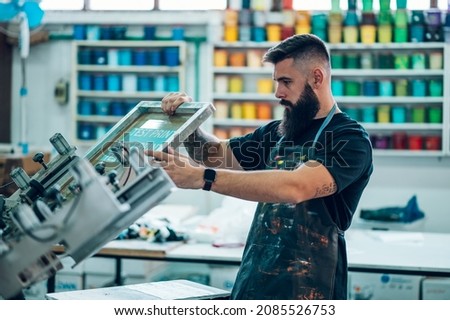 Male worker using screen printing film and a printing machine in a workshop Royalty-Free Stock Photo #2085526753