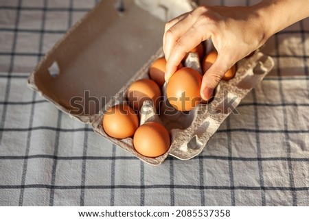 Chicken brown eggs are in a cardboard box bought at a grocery store. Healthy breakfast. A tray for carrying and storing fragile eggs. Woman takes one egg out of the package with her hand