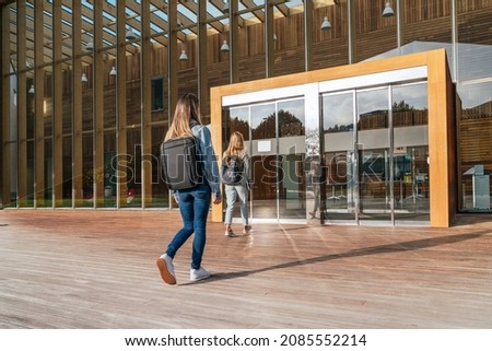 Rear view of two unrecognizable college students entering the university to attend classes on a sunny day. Royalty-Free Stock Photo #2085552214
