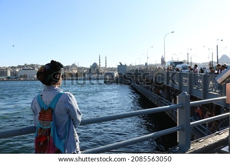 Young beautiful traveler girl in turban with backpack is watching a map near galata bridge in istanbul - famous view of Istanbul. Travel, tourism, excursion. tourist woman from arabia in turban